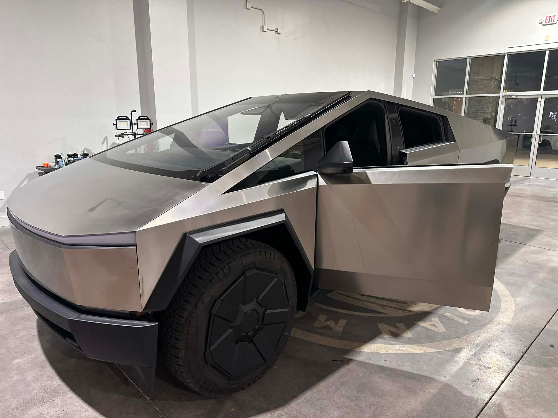 Tesla Cybertruck with open door, parked in a garage with concrete floor.