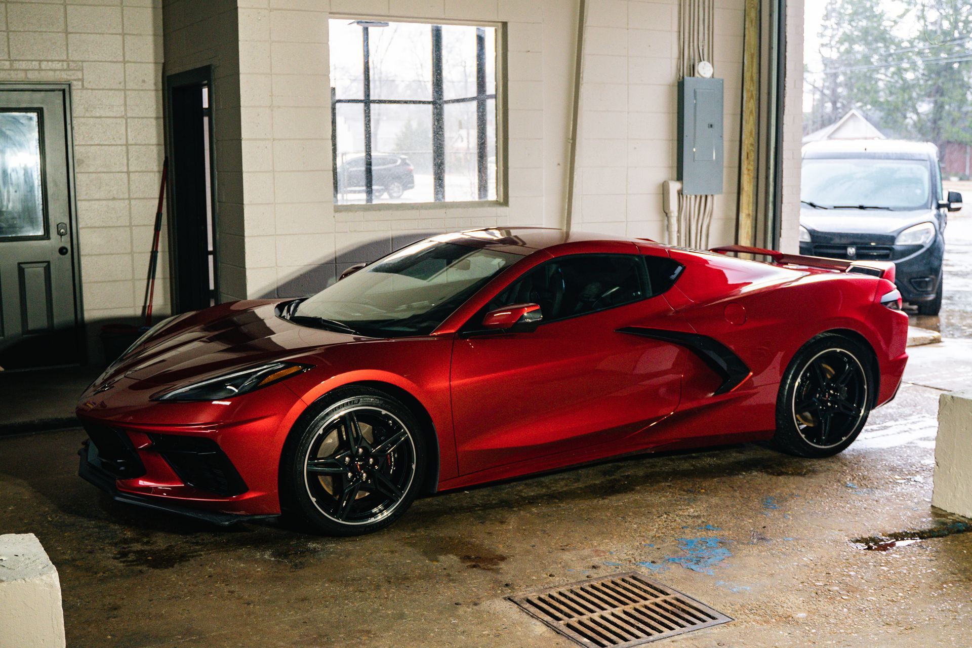 Red Corvette in a car wash bay. Black rims, shiny paint.