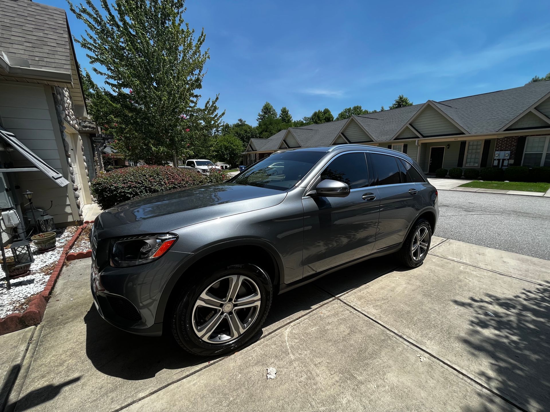 Gray Mercedes SUV parked on a paved driveway in front of a house on a sunny day.