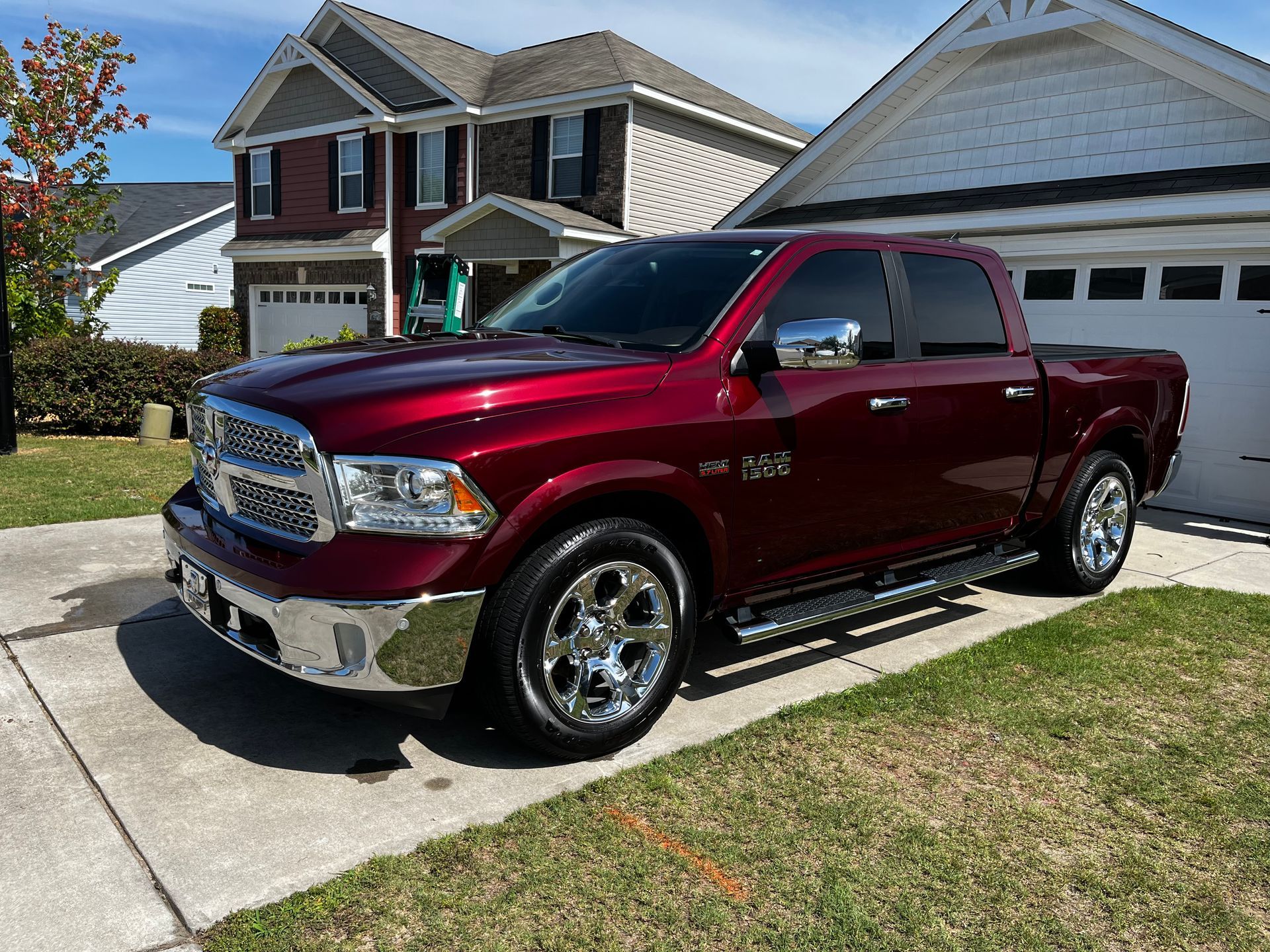 Red Dodge Ram pickup truck parked in front of a house. Shiny chrome accents, sunny day.