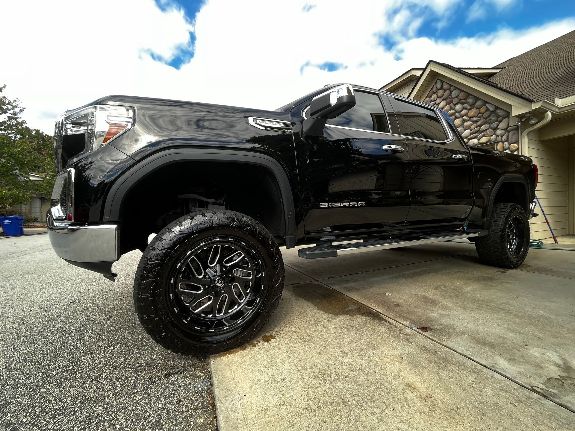 Black lifted GMC Sierra truck parked on a driveway with custom wheels, with a house in the background.