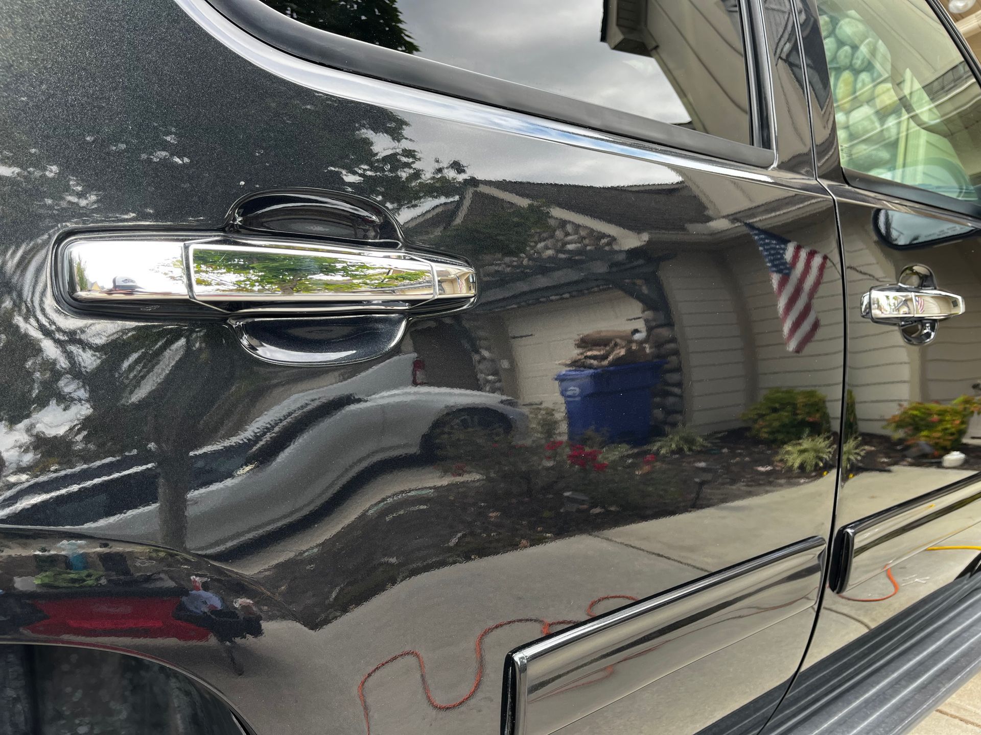 Shiny black truck door with chrome handle, reflecting a house and surroundings.