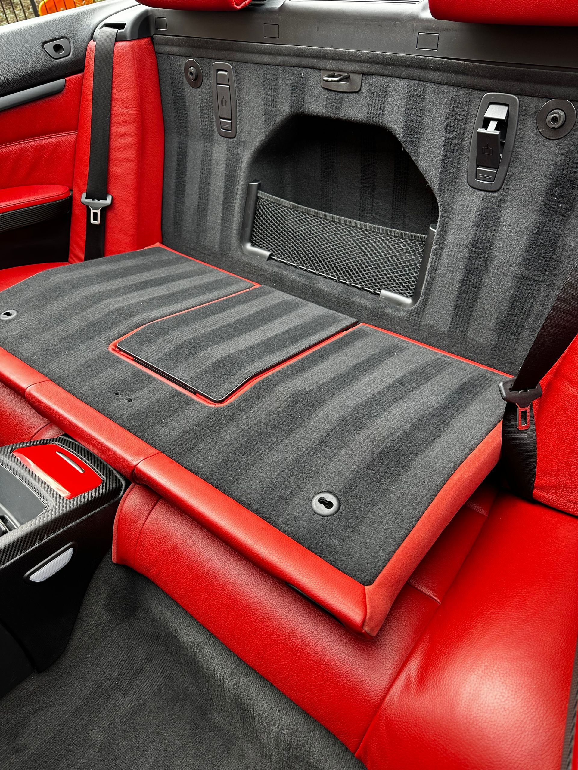 Red and gray car interior detail, showing the back seat with carpeted surfaces and red leather trim.
