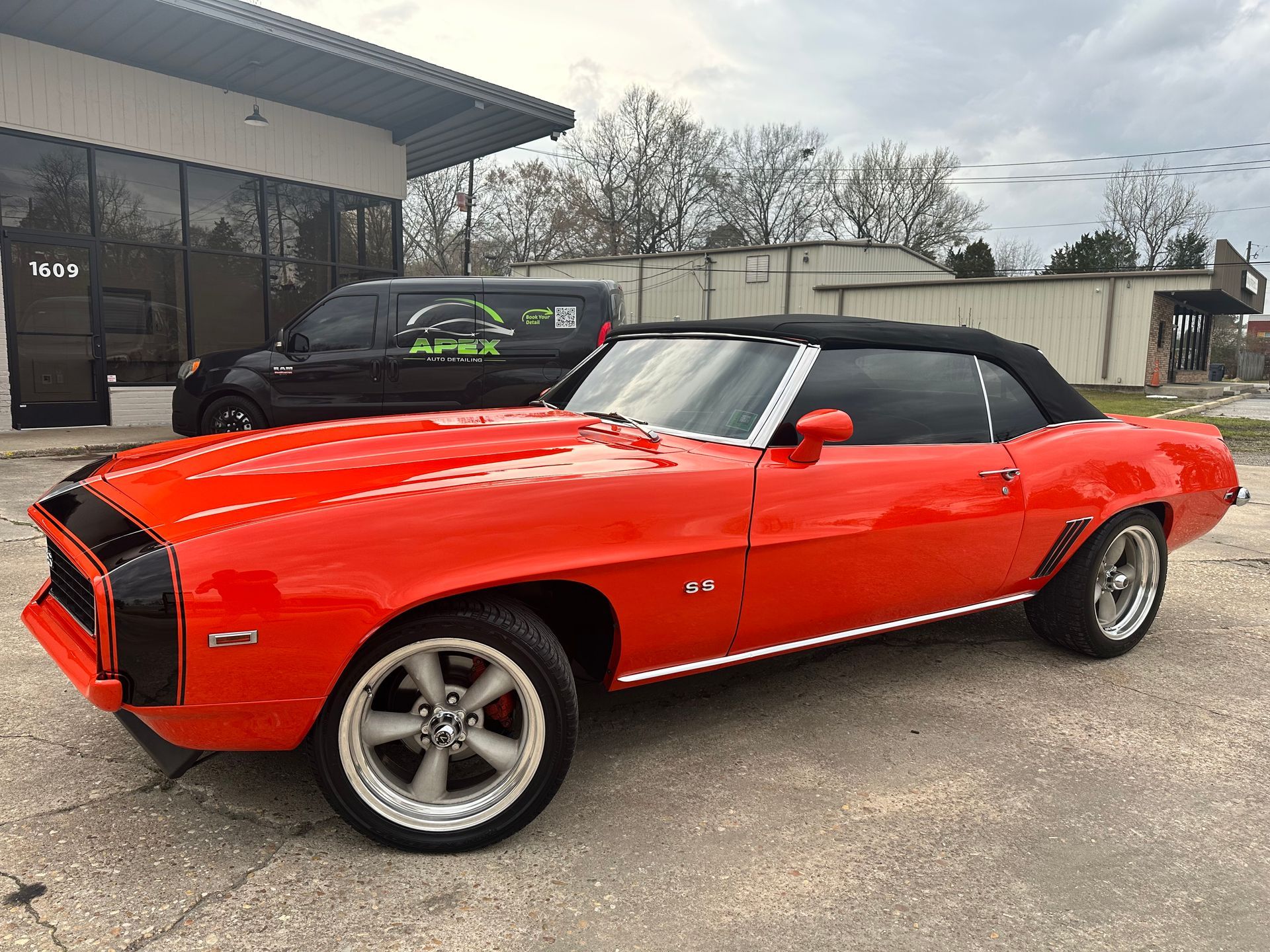 Bright orange convertible Camaro with black accents parked outside a business.