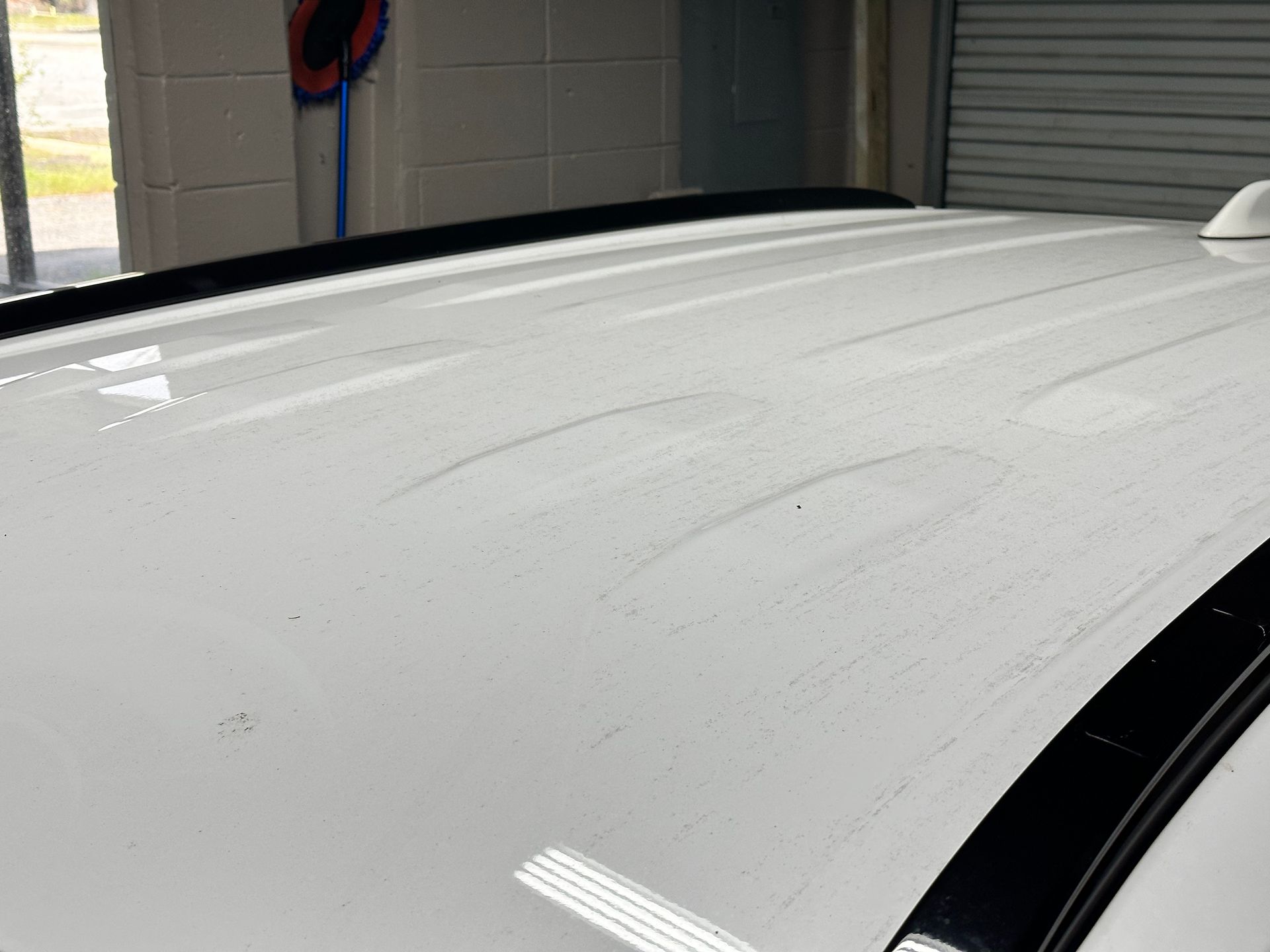 White car roof with wet streaks, showing cleaning, in a garage setting.
