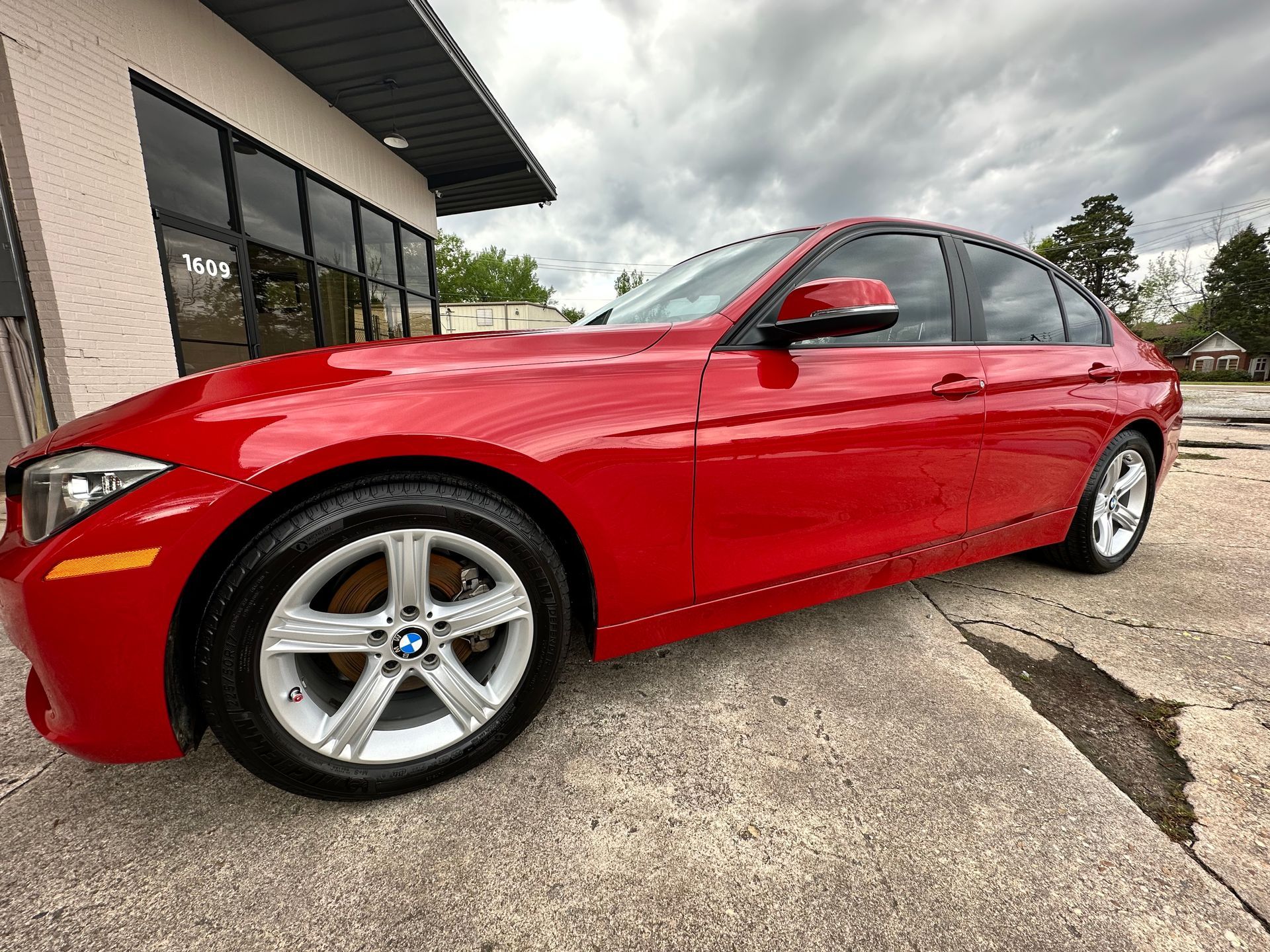 Red BMW sedan parked on a concrete surface in front of a building with large windows.