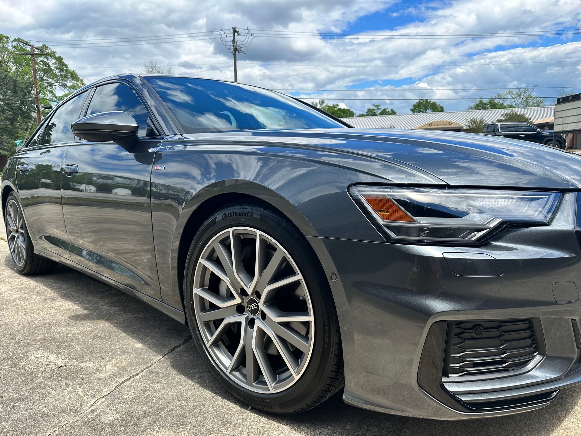 Gray Audi sedan parked on a concrete surface under a cloudy blue sky.
