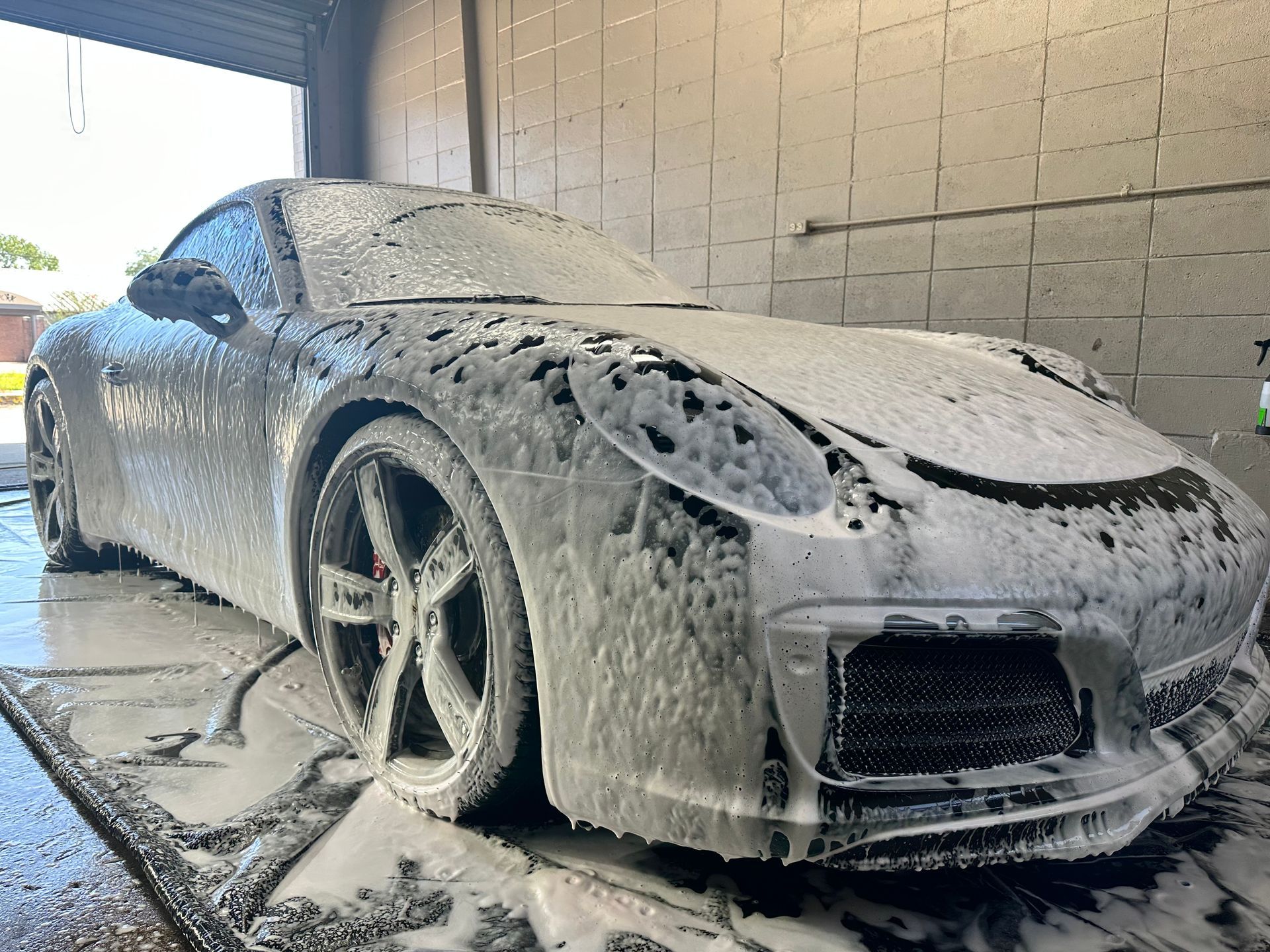 Silver sports car covered in foamy soap at a car wash.
