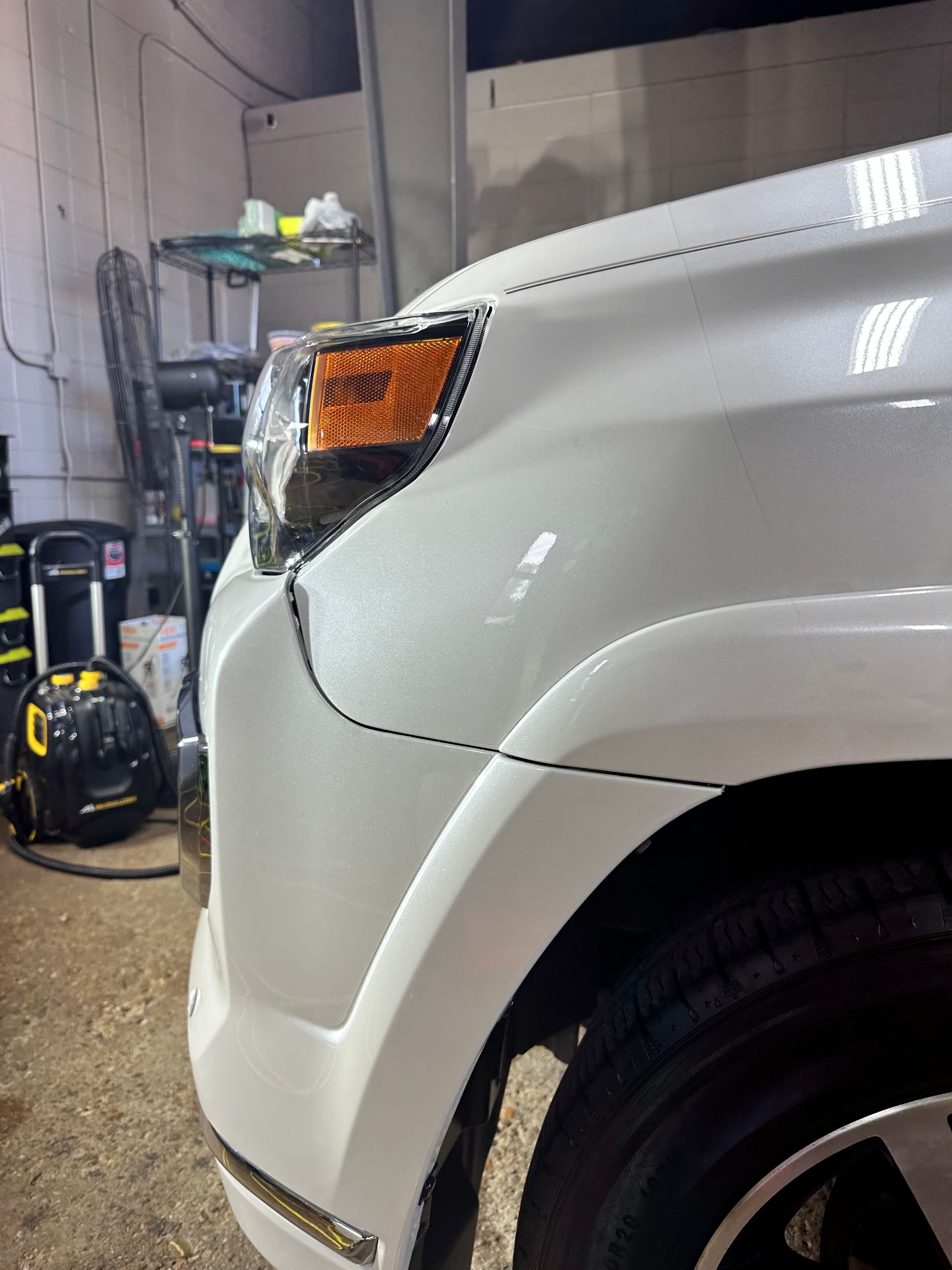 White car front quarter panel with orange turn signal in a garage setting.