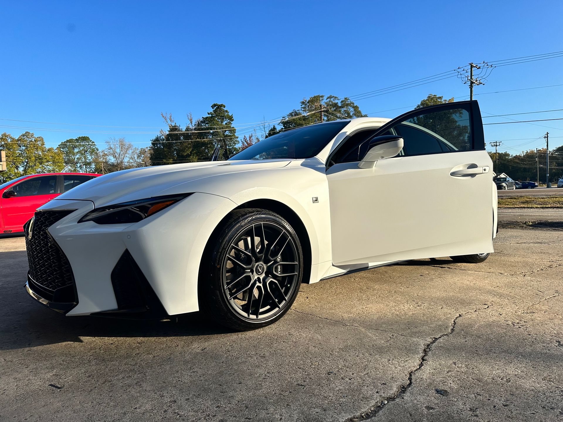 White Lexus sports car with black rims, parked with driver's side door open, under a blue sky.