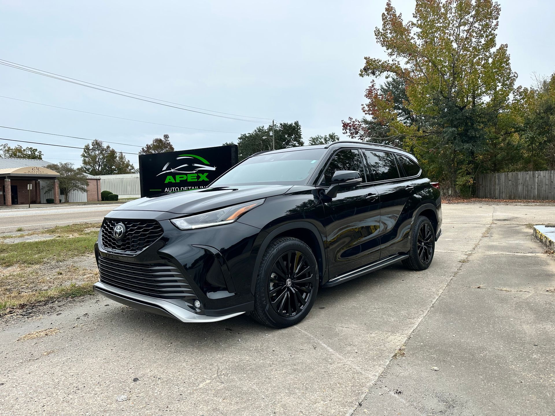 Black Toyota Highlander SUV parked on concrete with Apex sign in the background.