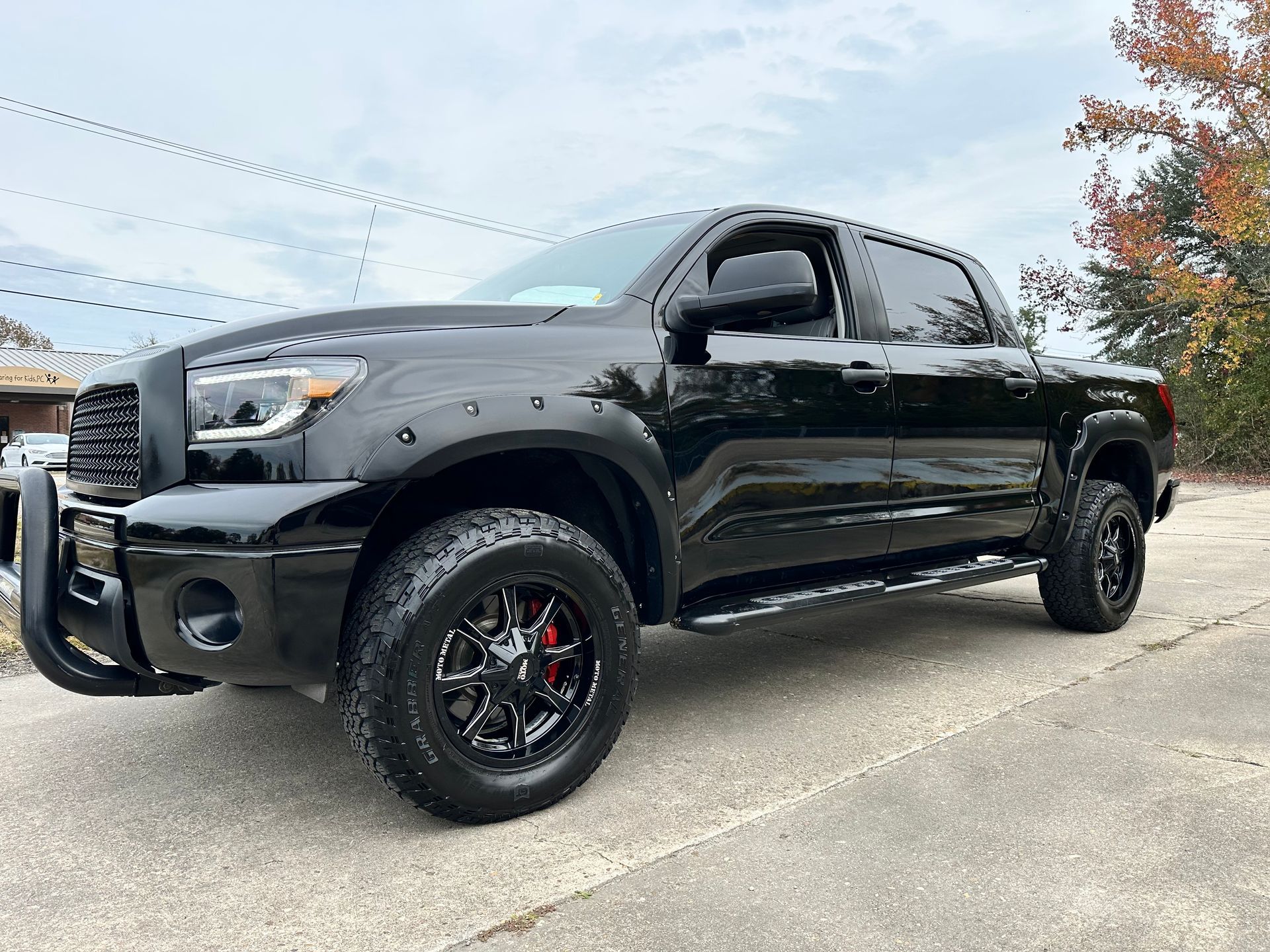 Black Toyota Tundra pickup truck with black wheels and brush guard, parked on a paved road.