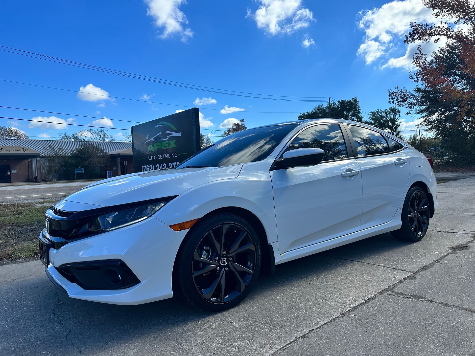 White Honda Civic hatchback parked on a street in front of a business with a green sign on a sunny day.