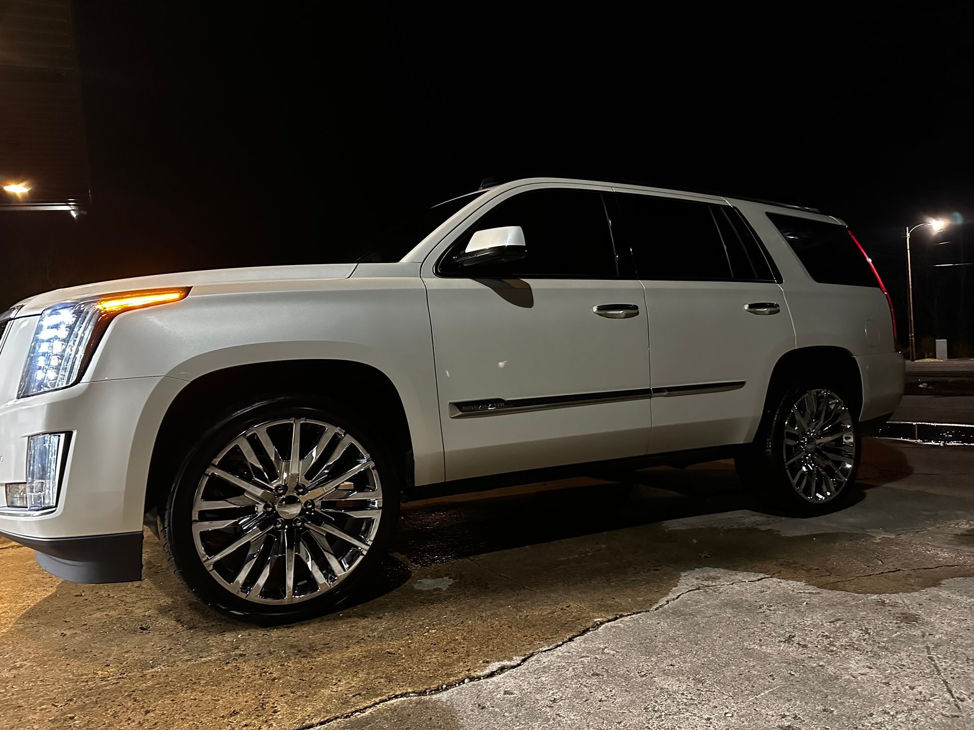 White Cadillac Escalade SUV parked at night with chrome rims.