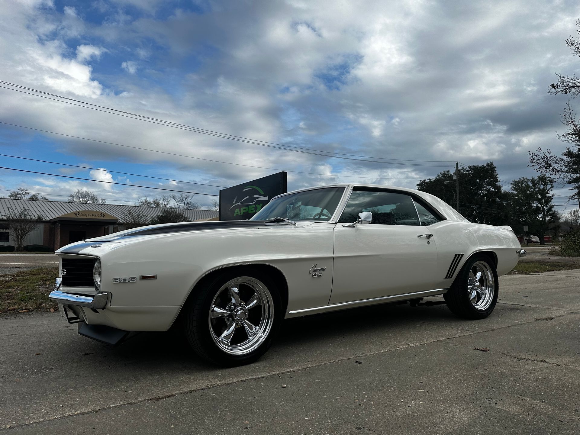 White 1969 Chevrolet Camaro with black stripe and chrome wheels parked on pavement against cloudy sky.