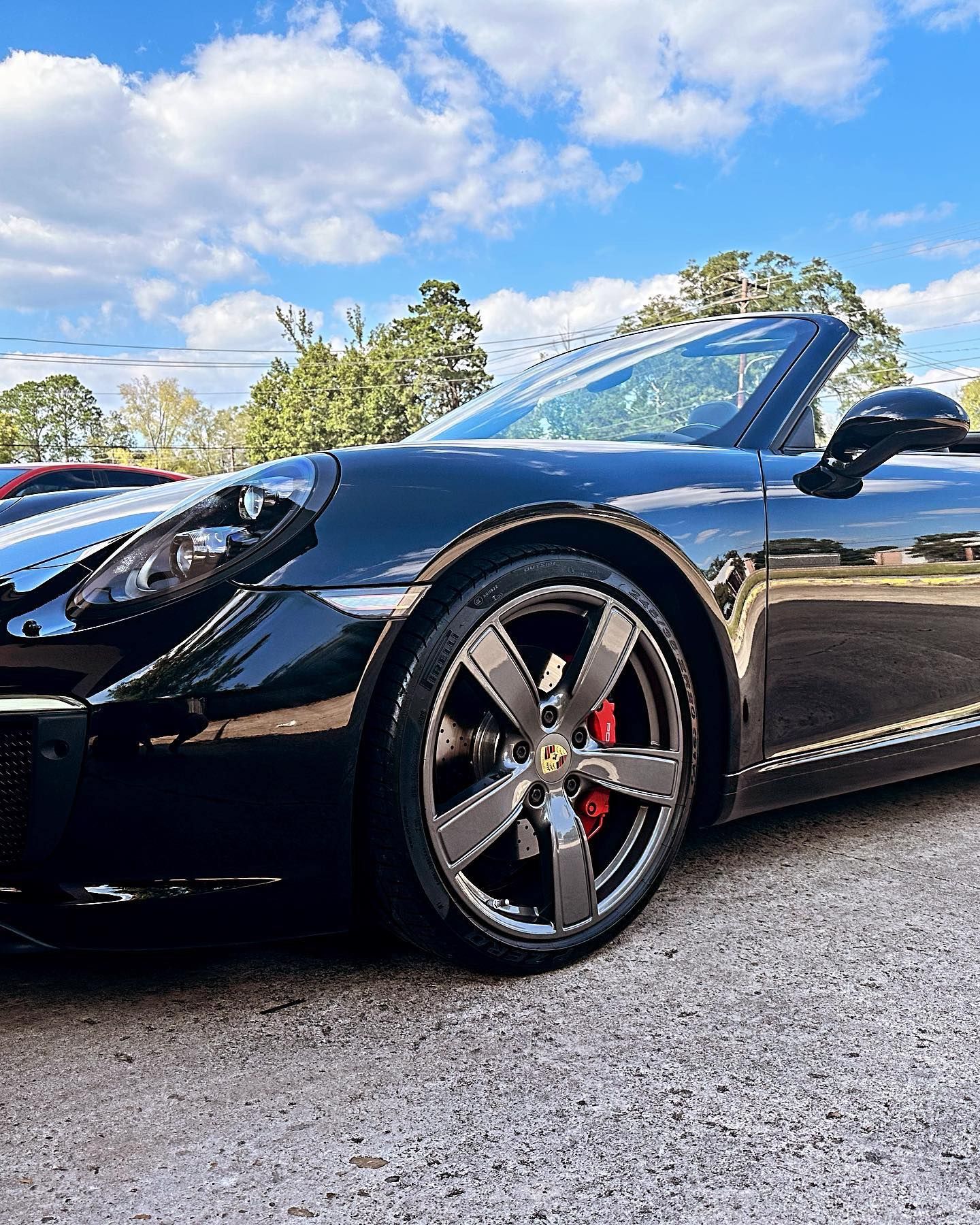 Black Porsche convertible with silver rims, parked outdoors on a cloudy day.