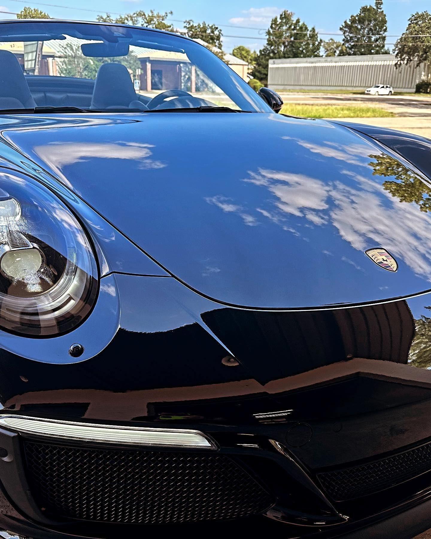 Black Porsche convertible with a shiny hood reflecting the sky.