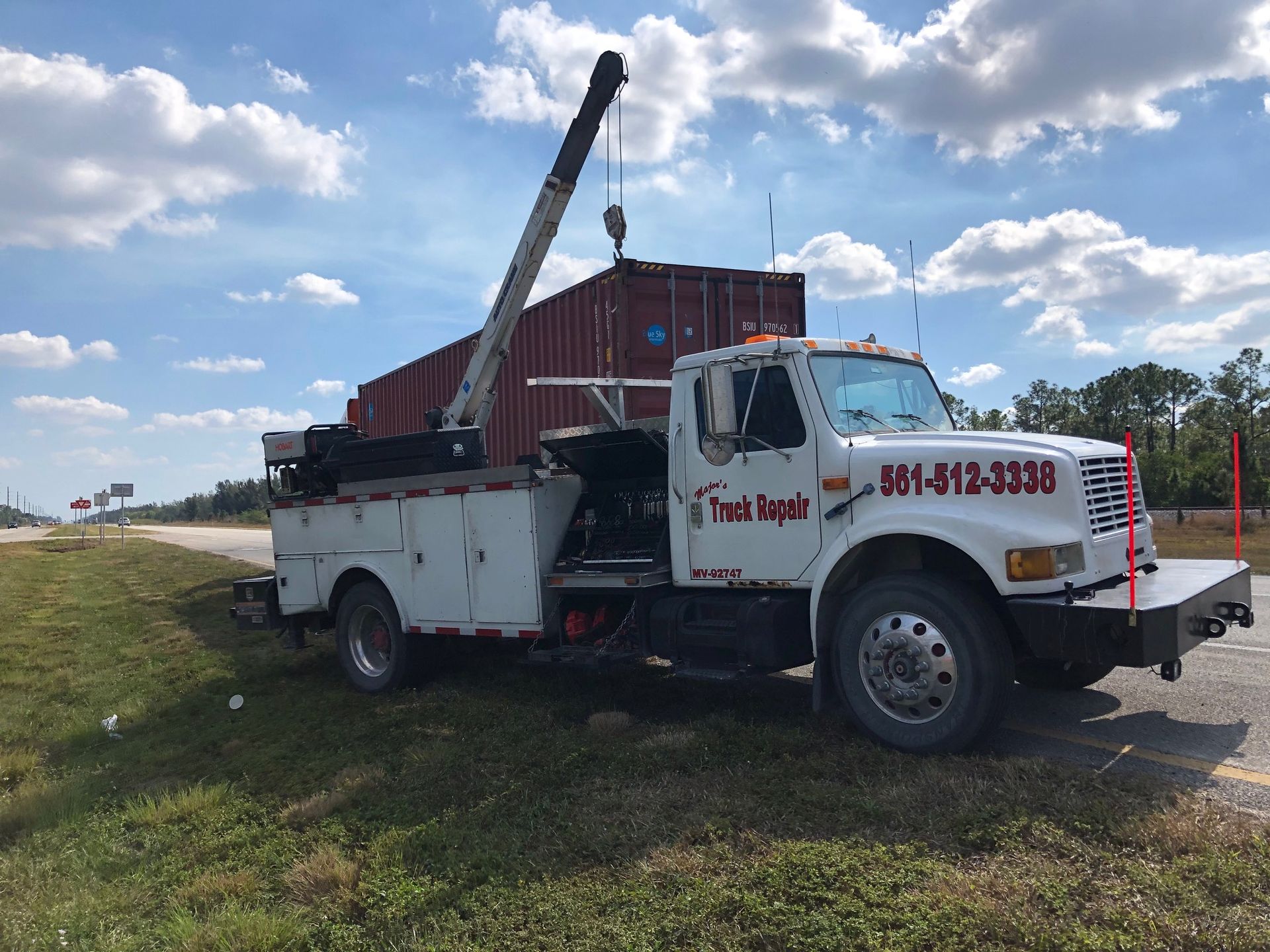 A tow truck with a crane attached to it is parked on the side of the road.