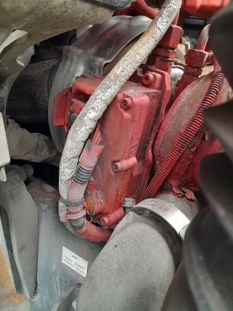 Red engine component with various tubes and wires, in a truck engine bay.