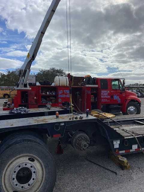 A red tow truck with a crane attached to it is parked in a parking lot.