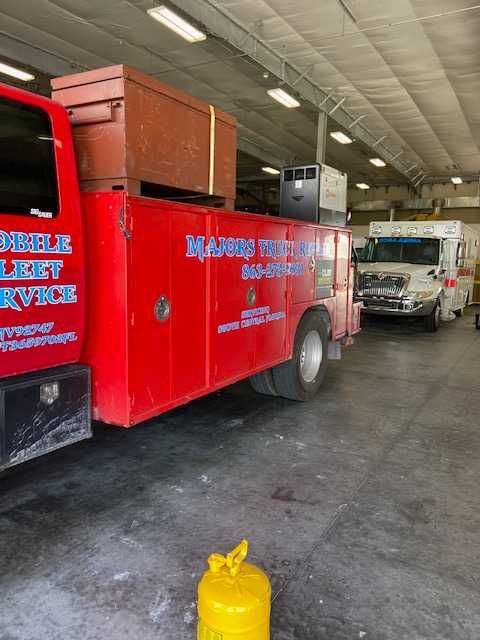 A red truck is parked in a garage next to a white truck.