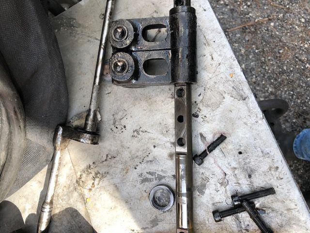 Disassembled mechanical parts on a dirty surface. Includes bolts, a long rod, and a bracket.