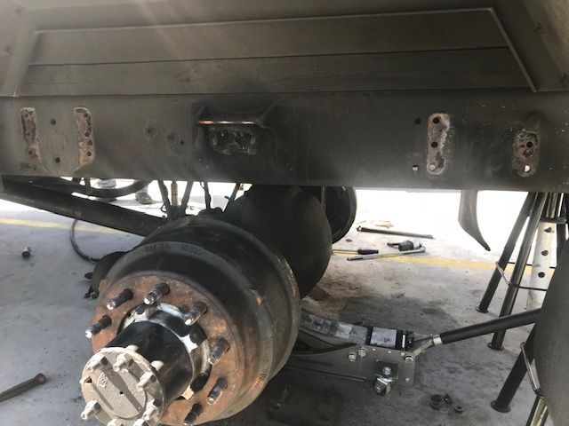 Undercarriage of a truck with an axle and frame visible. Welds and bolt holes are present on the frame.