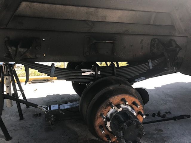 Trailer axle and leaf springs, supported by a jack and stands, undergoing repair.