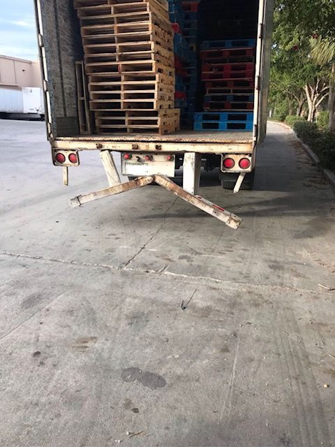 Open truck with stacked pallets; damaged loading ramp. Concrete ground, outdoor setting.