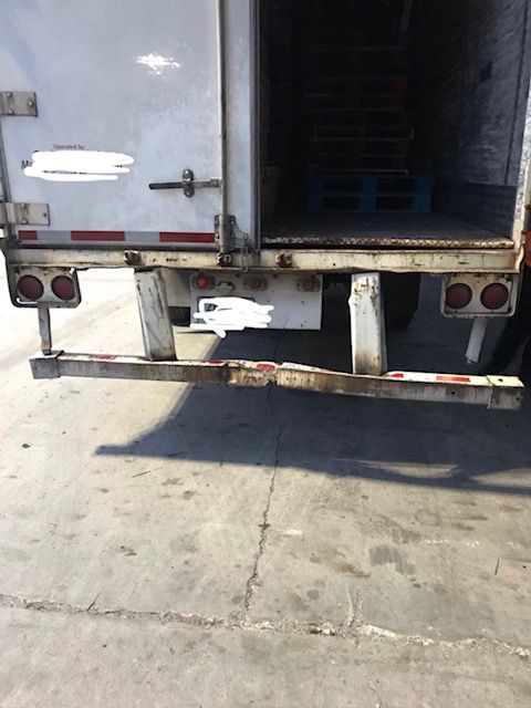 Rear of a semi-trailer truck with open doors, revealing an empty cargo area with wooden pallets.