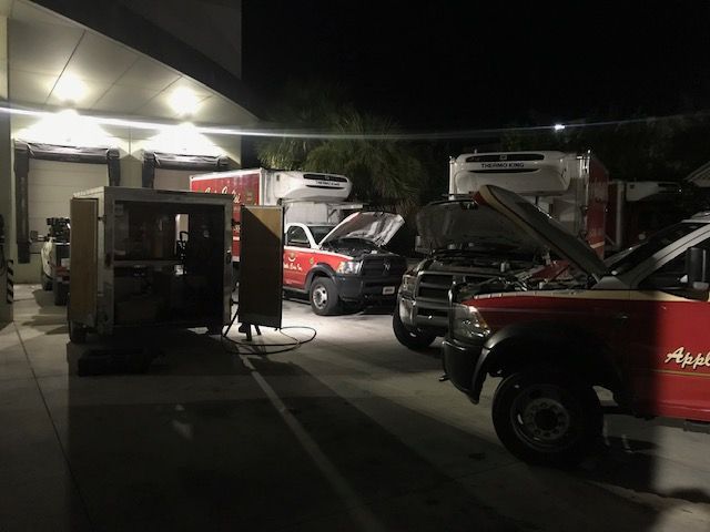 Red work trucks parked at a loading dock at night. Some have open hoods, and a generator is running.