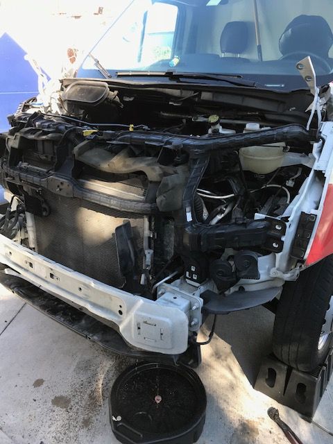 A white van's front end is dismantled, revealing engine components. Outdoors.