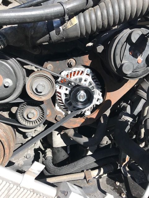 Engine with a new alternator installed, visible belts, pulleys, and various components.