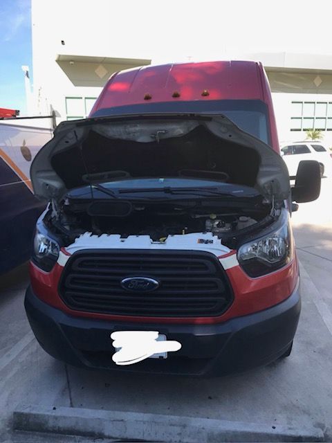 Red Ford Transit van with hood open, parked in a lot.