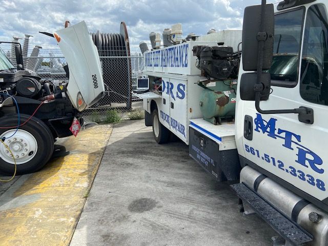 White service truck with raised hood, parked outdoors near a fence. The truck has the logo 