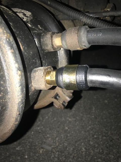Two air brake hoses connected to a vehicle's brake component with brass fittings and rubber hoses.
