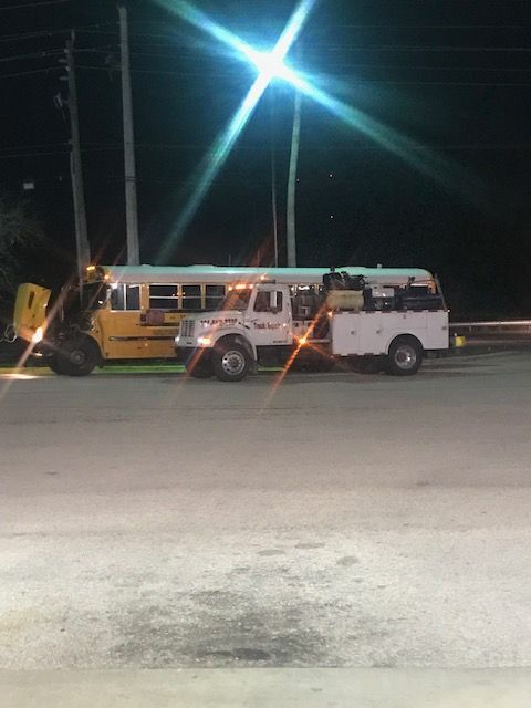 Yellow school bus and white service truck parked at night under a bright streetlight.