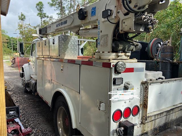 White utility truck with crane boom extended, parked outdoors.