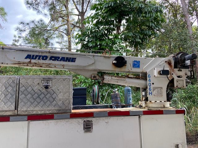 White utility truck with an Auto Crane boom, in a wooded area.