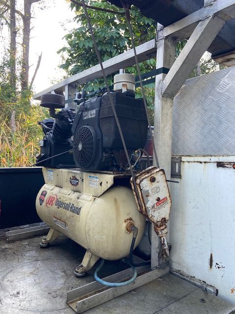 Air compressor with attached engine and jackhammer, outdoors.