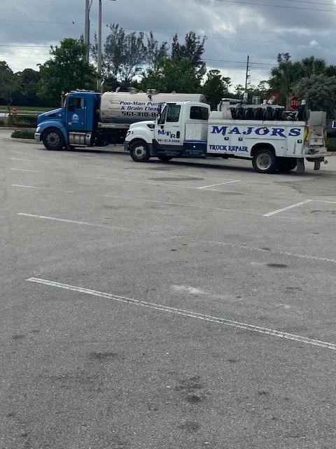 Two trucks parked in an empty parking lot, one blue tank truck and one white service truck.