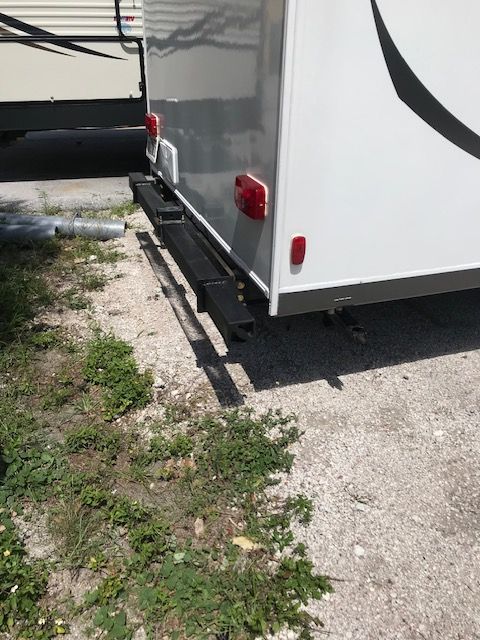 Black step below the back of a white RV. Red taillights are visible.