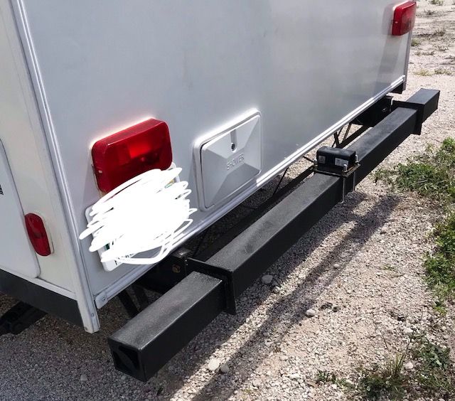 Rear view of a white camper with a black bumper, red taillights, and a small white storage compartment.