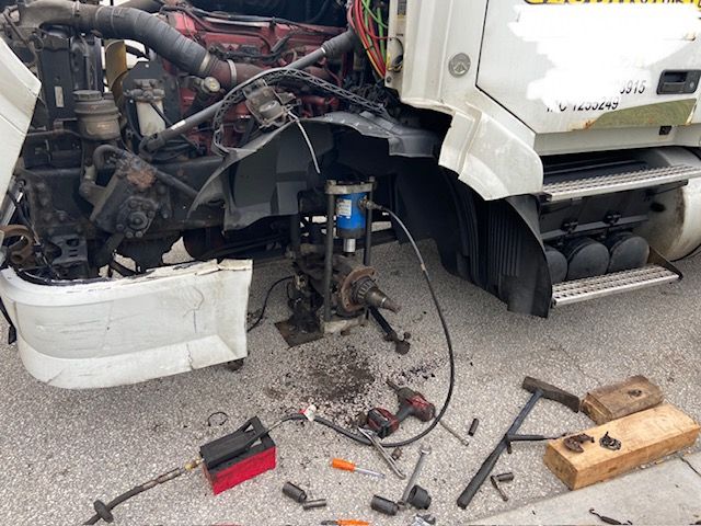 Semi-truck being repaired; damaged front wheel well with tools scattered on pavement.