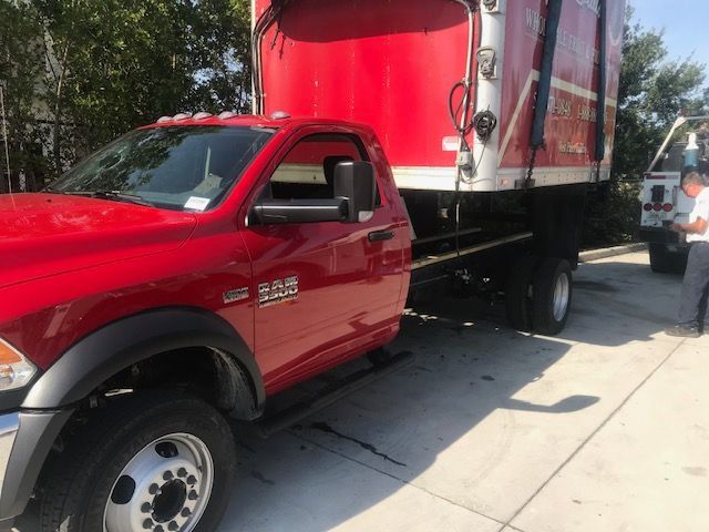 Red Ram 5500 truck hauling a large red and white refuse container on a paved lot.