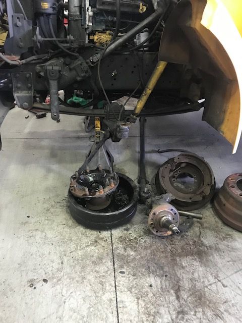 Truck front end repair. Axle, brake drums, and other parts are removed on a shop floor.