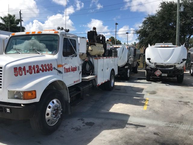 White work trucks with open hoods parked outside, phone number on the side of first truck.