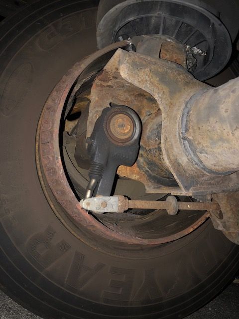 Close-up of a rusty truck wheel with a black sensor and brake components visible.