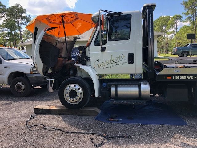 Tow truck with open hood, umbrella, and a spill on a mat. White truck in front of a house.