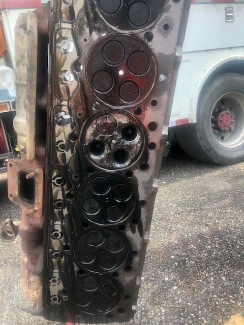 Engine cylinder head with black valves, covered in oil, outside.